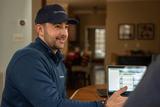 A man in a blue jacket and cap smiles while explaining old home foundation repair with examples on his laptop at the table.