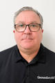 A man with short gray hair and glasses wearing a black "Groundworks" polo shirt, facing forward.