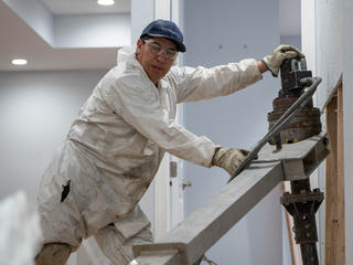 A worker in protective gear operates construction equipment indoors, taking measures to prevent soil erosion, with gloves and safety glasses.