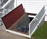 Cellar doors open outside a white house, revealing concrete steps—ideal for those needing bilco door repair or maintenance.