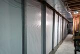 A basement wall with white plastic vapor barrier, metal support beams, and insulation along the unfinished ceiling.