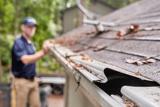 A person cleaning leaves and debris from gutters on a house roof.