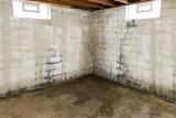 A basement corner with stained concrete floor and moldy, water-damaged cinder block walls from nor’easter basement flooding.
