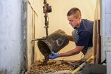 Man pouring rocks from a bucket onto the floor during construction or renovation work in a building.