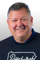 Smiling man wearing a black Pittsburgh sweatshirt against a gradient background.
