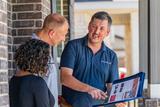 Three people stand outside by a brick wall, reviewing documents and photos on a clipboard.