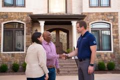 A man in a blue shirt shakes hands with another man outside a house after discussing foundation repair.