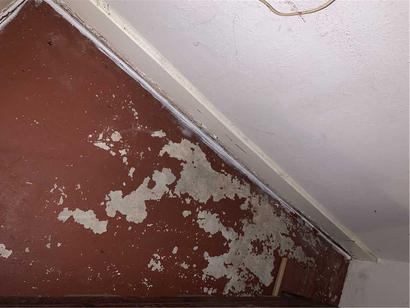Peeling paint on a brown wall and white ceiling in the corner of a room.