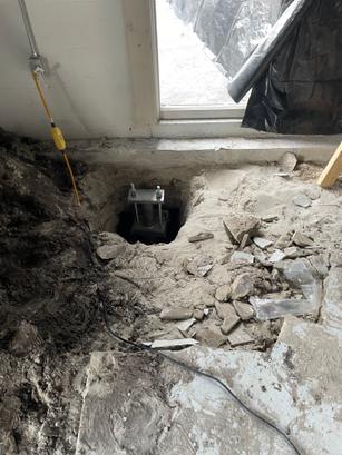 A hole in a concrete floor exposes a metal support bracket near a window during construction work.