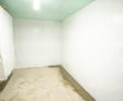 A small, empty, white room with concrete floors, a ceiling light, and a visible basement vapor barrier along the walls.
