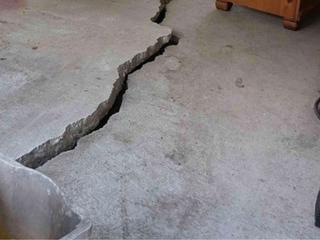 Large crack running across a concrete floor indoors, with some furniture visible nearby.