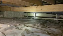 Crawl space with a plastic vapor barrier on the ground and sagging wooden beams overhead.