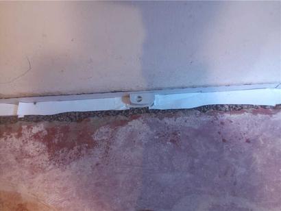 White strip with a plastic clip runs along a rough concrete floor next to a wall.