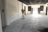 An empty, unfinished room with exposed ceiling, white walls, a standing fan, and light from open double doors.