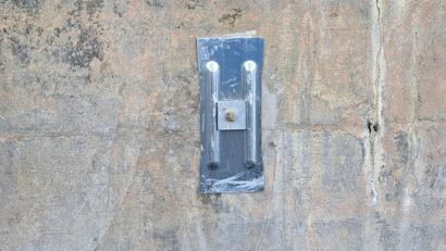 A metal wall hook with a single screw is mounted on a rough, weathered concrete wall.