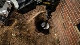 A mechanical auger drills a hole in the ground next to a brick wall, stabilizing the area near an uneven floor.