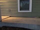 Cracked concrete porch slab in front of a house with green siding and a window above.