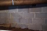 Cinder block basement wall with an obvious horizontal and stepped crack in the mortar joints, showing signs of white mold.