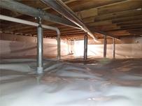 Crawl space with plastic vapor barrier covering the floor and plumbing pipes overhead.