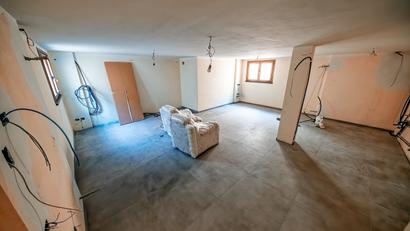 Large empty room under renovation with exposed wires, bare walls, a lally column, and two covered chairs in the center.