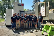 Group of people in matching T-shirts standing in front of a construction site under a clear blue sky.
