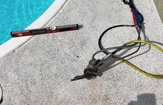 A cracked poolside patio with a level tool and repair equipment lying on the concrete surface.