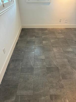 Gray rectangular floor tiles with white streaks in an empty room with white walls and baseboards.