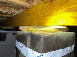 Wood beam resting on stacked wood blocks atop a padded column in a basement, lit by a flashlight.