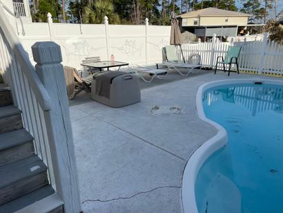 A backyard pool with loungers, chairs, stairs, and a white fence with fish designs on a sunny day.
