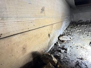 Close-up of a wood foundation with cracks and loose debris on the ground nearby.