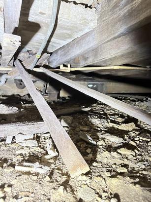 Dimly lit crawlspace with debris, exposed pipes, and wooden beams under a building structure.