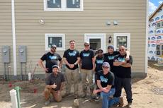 A group of people in work clothes poses in front of a house under construction.