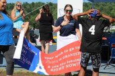 A boy in a black "4" jersey reacts with joy as adults reveal a "Make-A-Wish Paris" banner outdoors.