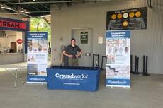 Person standing at a Groundworks booth with informational banners inside a baseball stadium