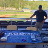 Groundworks member standing at booth in front of baseball field