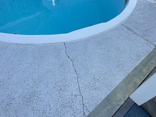 A crack runs through the concrete surface next to a swimming pool.