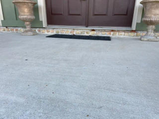 Two large planters flank a double door entrance with a black doormat on a concrete porch.