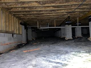 A crawlspace with exposed insulation, concrete block supports, and plastic sheeting on the ground.