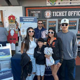 A group of five people posing and smiling in front of a ticket office at a sports venue.