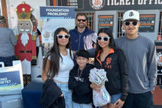 A group of five people posing and smiling in front of a ticket office at a sports venue.