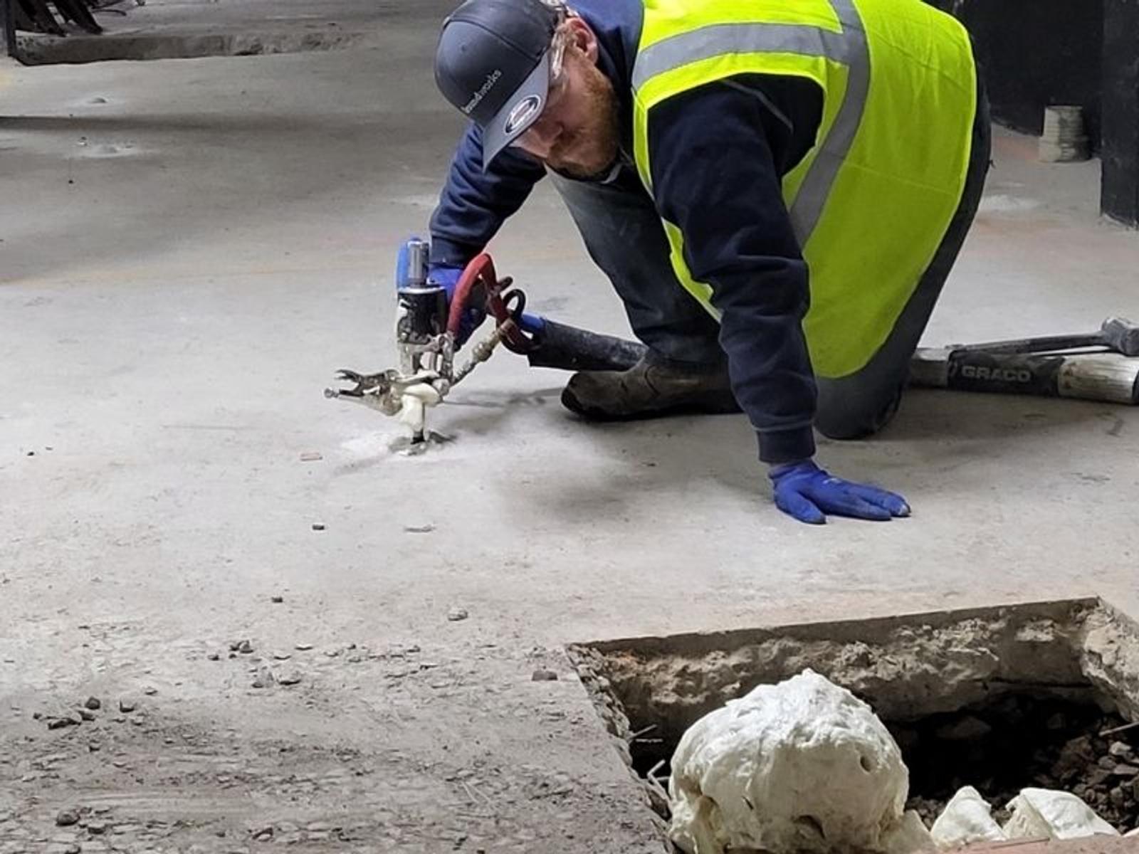 Image of Groundworks Commercial technician injecting hydrophobic polyurethane to stabilize slab on grade and fill voids in soil inside of a parking garage