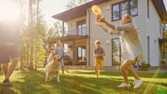 family and dog playing frisbee in front yard of house