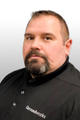 A man with short hair and a goatee wearing a black "Groundworks" shirt against a light background.