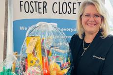 Smiling woman holding a gift basket in front of a "Macomb Foster Closet" sign.