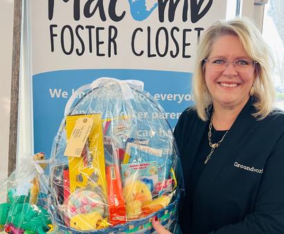 Smiling woman holding a gift basket in front of a "Macomb Foster Closet" sign.