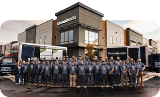 A large group of people in matching shirts stand in front of a Groundworks office building and branded trucks.