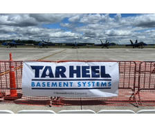 Four fighter jets parked on a runway behind a fence with a "Tar Heel Basement Systems" banner.