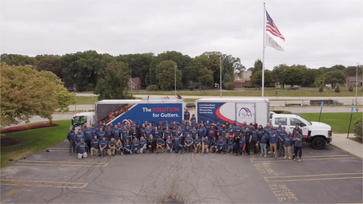 A large group of people in matching shirts pose in front of two company trucks in a parking lot.