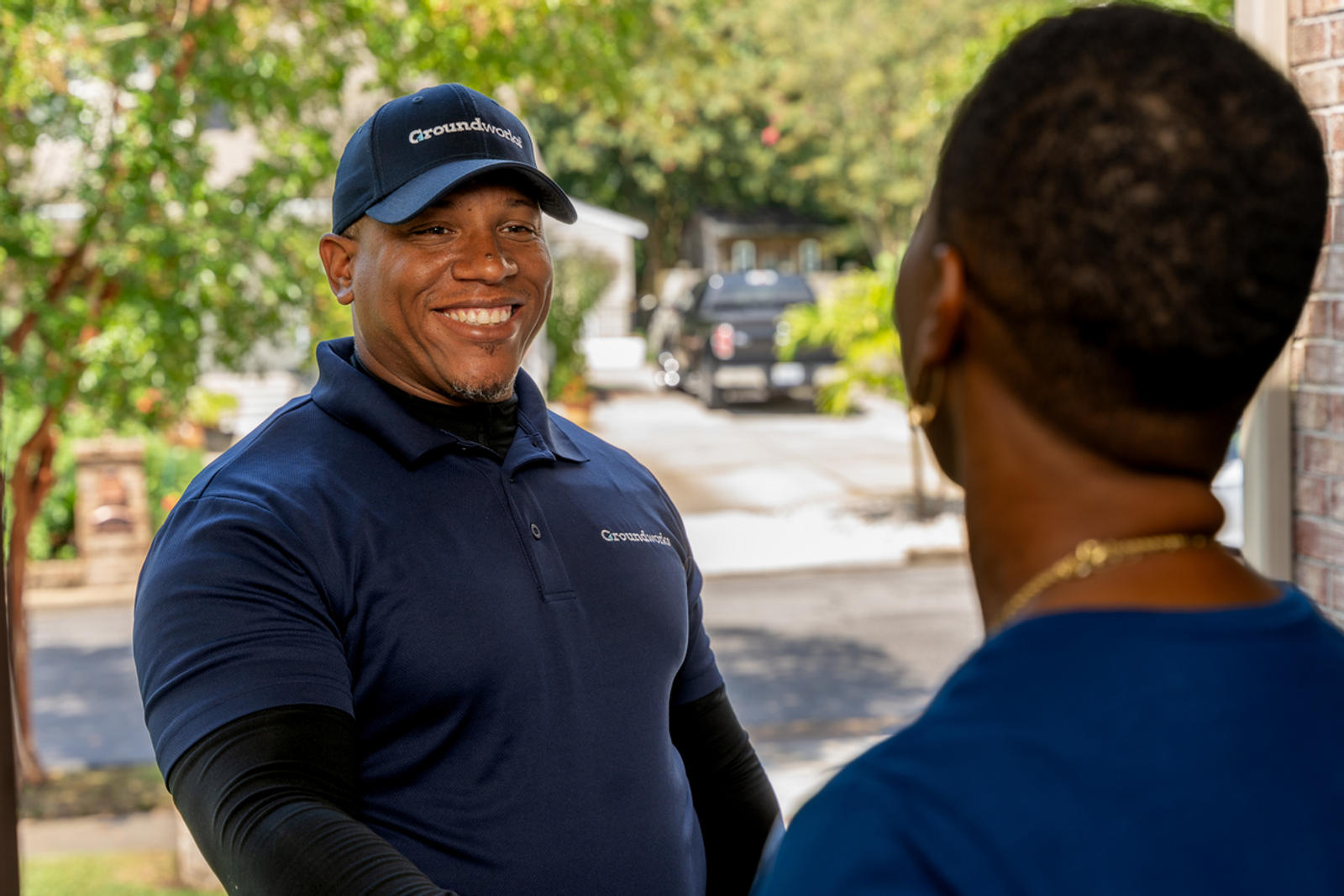 Smiling delivery worker in uniform greets a customer at their doorway in a suburban neighborhood.