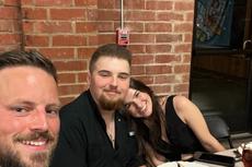 Three people smiling at a table with empty plates in a restaurant with brick walls and a window behind them.